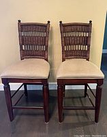 Full front view of the two wooden dining chairs with woven backs and beige fabric upholstered seats, side by side.
