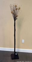 Full view of tall black metal floor lamp with multiple thin rods radiating upward from the top, set against a wall with baseboard.