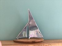 Front view of the decorative sailboat showing metal sails on a wooden base with a smooth turquoise background.