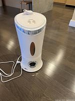 White Honeywell humidifier photographed from the front and side, showing water window, control dial, and power cord on a wooden floor.