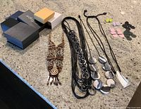 Lot of artistic jewelry including boxed items, three necklaces, and multiple pairs of earrings arranged on a countertop.