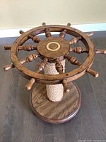 Side table photo showing nautical captain wheel design with 8 handles and brass center detail, placed on dark floor.