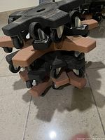 Stack of seven black and brown plastic roller plant bases with swivel casters on tile floor