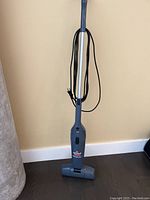 Full view of the small upright Bissell Magic Vac vacuum cleaner showing handle, power cord, and base unit against a light-colored wall and floor.