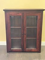 Front view of wooden cabinet with glass doors showing two shelves inside and wooden back panel.