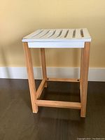 Angle view of wooden plant stand showing natural wood frame and white slatted top with water damage.