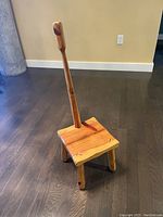 Solid wooden step stool with four legs and attached vertical handle, photographed on a hardwood floor against a beige wall.