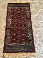 Full view of Greek wool rug showing red patterned front and beige fringe end.