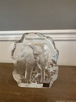 Front view of clear lead crystal sculpture depicting an elephant standing amid textured foliage with an irregular outline.