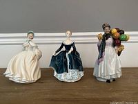 All three Royal Doulton figurines side by side on a wooden surface against a gray background.