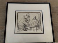 Framed etching depicting three men seated around a table, signature visible at the bottom right