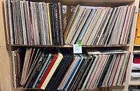 Two wooden shelves filled with classical LP vinyl records on top and bottom rows