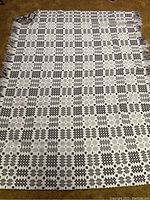 Full view of coverlet laid flat showing beige background with brown geometric pattern and fringed edges.