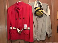Full view of reenactment outfit including red jacket, khaki shirt, cream belt, and yellow-blue satchel bag hung on a door.