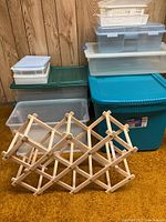 Front view of stacked plastic storage totes and smaller bins, plus the folding wood wine rack front and center