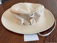 Front and side angled view of white wide-brim hat with crown and sewn brim, chin strap, and metal ventilation eyelets.