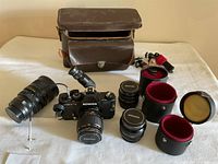 Full lot overview showing camera, lenses, leather case, and accessories spread on table.