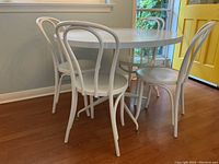 Corner angle view of round white table with four bentwood style chairs.