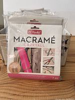 Front view of the Macrame Carryall starter kits in original sealed packaging showing Kit Market branding and project preview images.