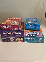 Photo of six board games stacked including Yahtzee, Killer Bunnies, What's Yours Like?, Catch Phrase, Beyond Balderdash, and SpongeBob Kids Cranium.