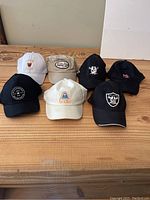 Seven assorted caps laid on wooden table, showing front logos and style variety