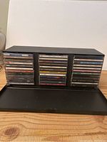 Black rectangular CD holder case with 36 CDs stored inside on a wooden surface.