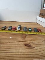 Eight die-cast cars placed side by side with measuring tape approximately 9 to 20 cm long each.