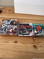 Photo of the three game boxes pictured together on wooden surface showing lot contents: Stratego Original, Redbird Aeroplane model, MasterChef board games