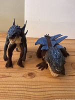 Two Godzilla character dolls placed on a wooden surface, one standing and one in four-legged pose