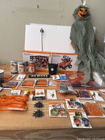 Wide view of the table with Halloween items displayed including decorative bulbs, earrings, cookie cutters, spider decorations, and packaging showing a Halloween-themed wagon toy.