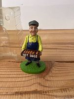 Front view of figurine showing vendor holding hot dogs tray.