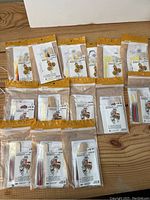 Overview of 14 sealed Color-in Puppet Kits laid out on a wooden surface showing varied designs and packaging from Creatology brand.