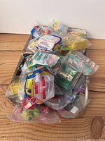 Pile of 28 McDonald's toys, all individually sealed in plastic packaging, placed on a wooden surface.