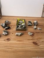 Overview of 17 mineral specimens arranged on a wooden surface with some in a small cardboard box. Various shapes and mineral types visible.