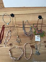 Overview photo showing nine assorted necklaces including shell, stone, and bead types laid on a wooden surface.