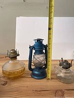 Photo showing three different oil lamps with a measuring tape indicating height of blue lantern is about 10 inches.