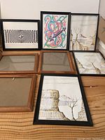 Eight picture frames arranged on a table, 5 with artwork including abstract and natural themes; frames are wood and black finishes.