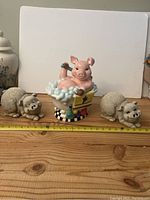 Front view of the pig in bathtub cookie jar with two ceramic pig figurines on each side, ruler for size reference