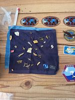 Pins spread on a blue cloth, various metal pins with aviation and smoking themes, plus three oval stickers reading 'NO SMOKING' and patches including an eagle patch.