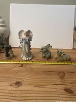 Front view of four ceramic statues displayed on a wooden surface. From left to right: deer, angel, rabbit, rabbit.