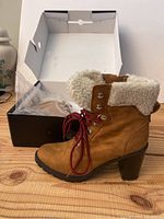 Photo of one tan lace-up women's boot with faux fur cuff and red laces, shown next to original box