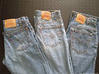 Three pairs of Levi's denim jeans folded at the knees showing back leather patches and pocket design, placed on black floor