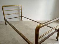Full view of brass headboard, footboard, side rails and center support in concrete-floored room
