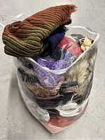 Clear plastic zipper bag filled with various clothing accessories including scarves, hats, and socks.