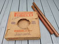 Cardboard box with Pirelli branding, partially torn, containing two heavy copper pipes next to it on a wooden surface.