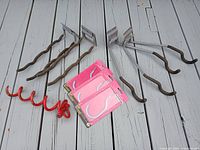 Six metal hangers with rubber-coated ends and three red screw-in hooks in packaging, along with a red corkscrew-shaped dog anchor on wooden floor.