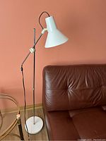 Full view of the white vintage adjustable floor lamp standing next to a brown leather chair and a glass table.
