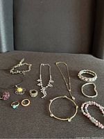 Clear overview of the lot consisting of 12 pieces of jewelry including necklaces, bracelets, and rings arranged on a dark fabric background.