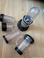 Magic Bullet blender base with multiple clear plastic blending cups and lids arranged on wood floor