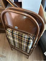 Two vintage Cooey metal folding chairs stacked together showing the back of the chairs with brown metal frames and plaid fabric backs.